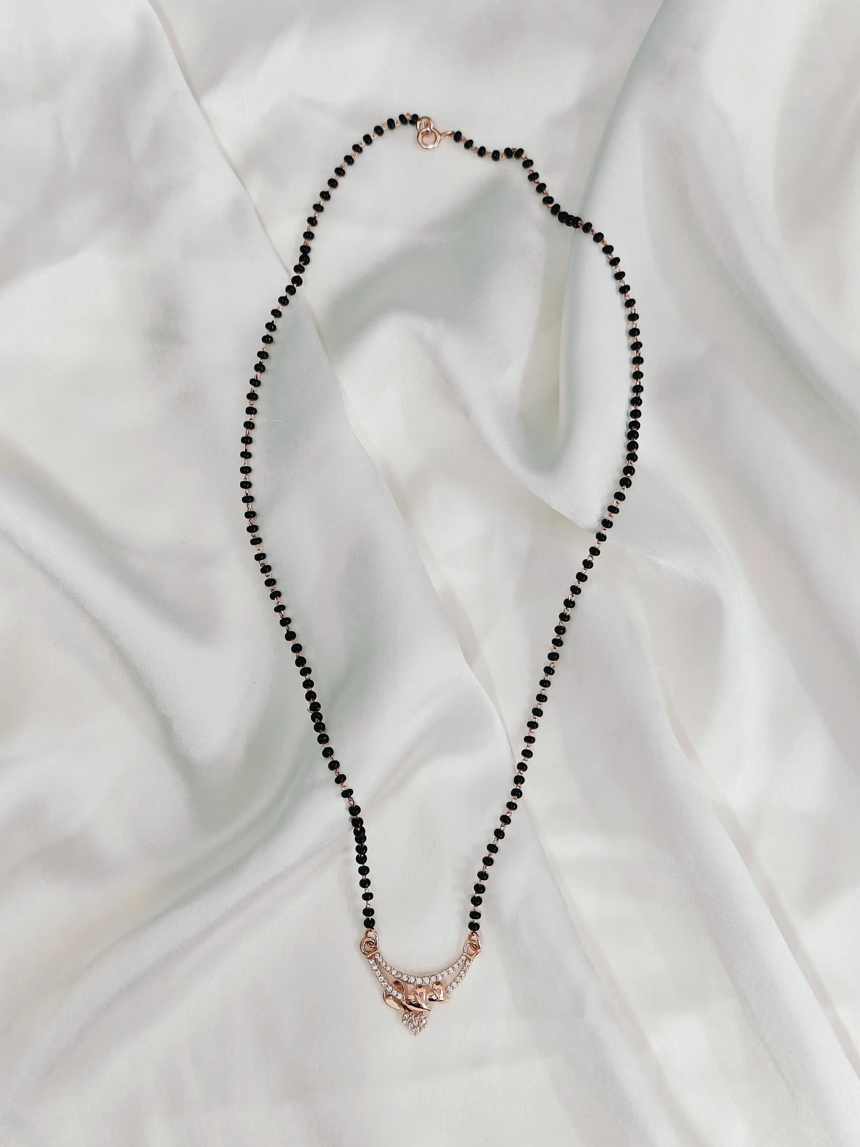 Black beaded necklace with a rose gold clasp on a white fabric background